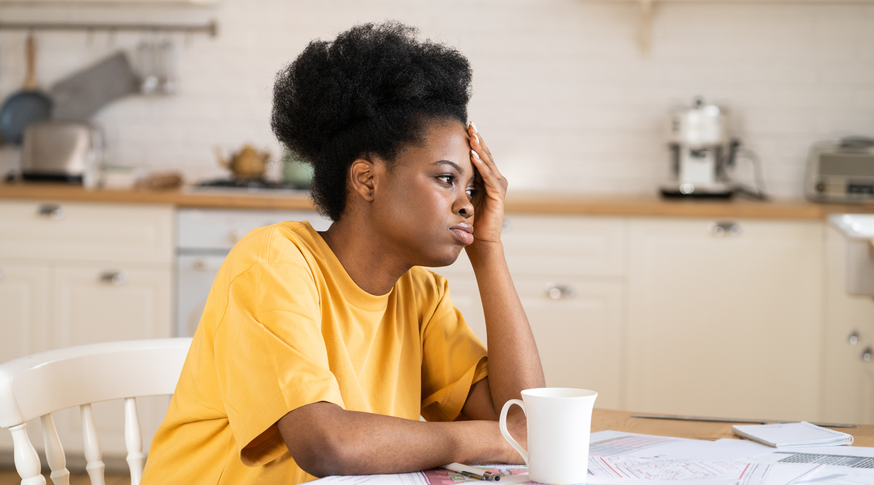Tired woman sits at the table with a coffee looking stressed
